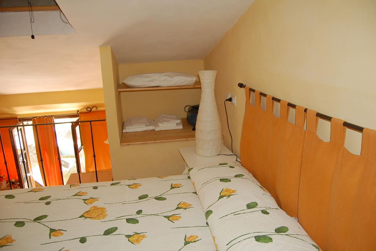 Ein Schlafzimmer mit einem Bett, einem Regal mit gefalteter Kleidung und einem Fenster mit Vorhängen.