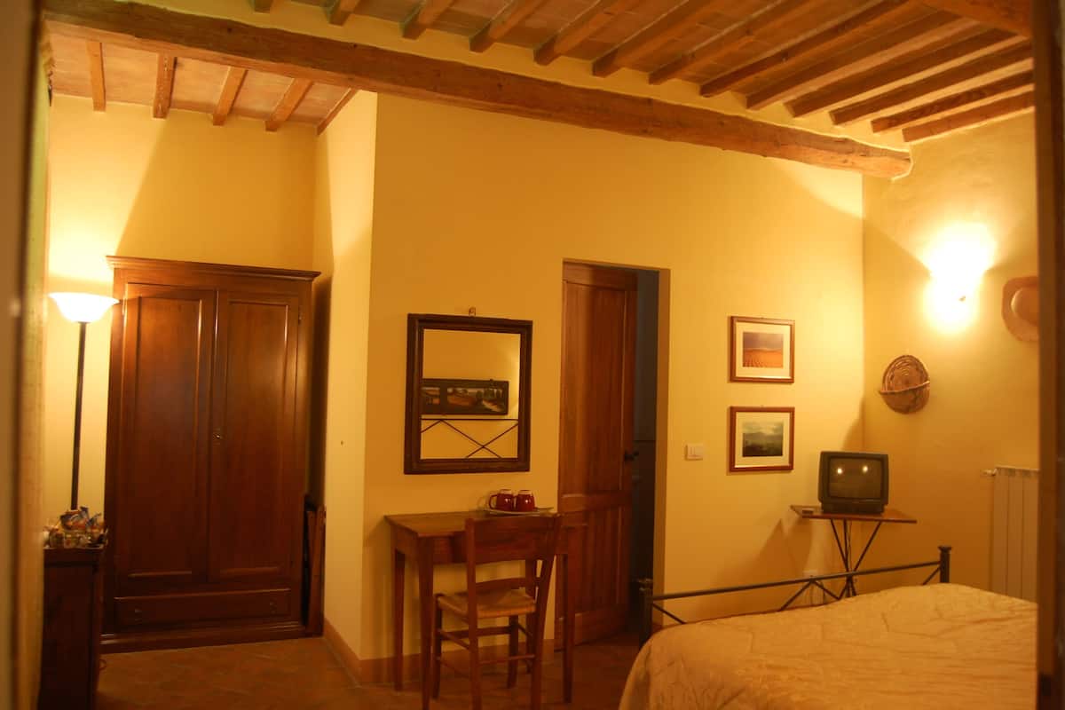 Ein Schlafzimmer mit einem Bett, einem Holztisch, einem Stuhl, einem Fernseher auf einem Schrank und einer Tür zu einem anderen Raum.