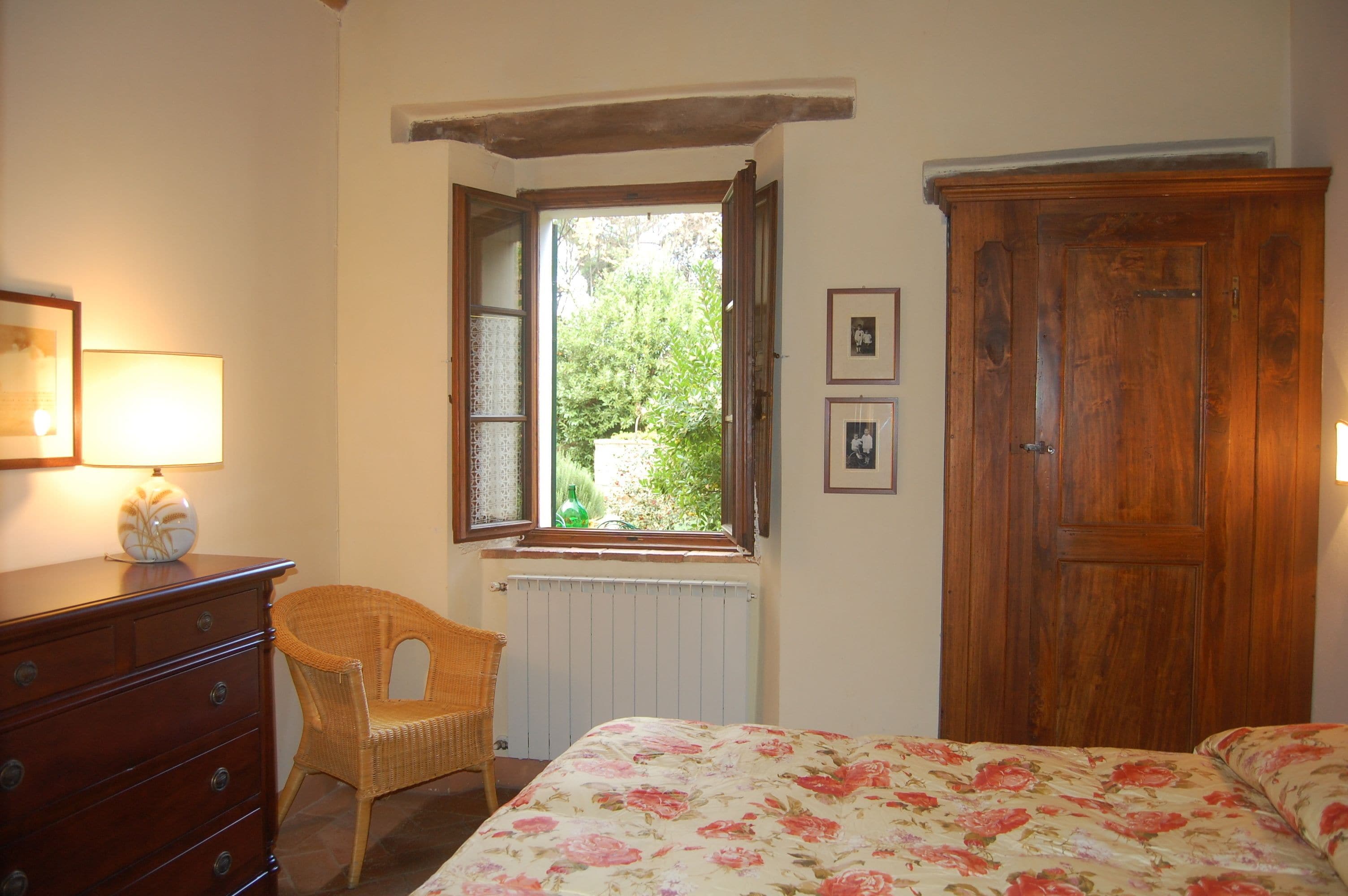 A bedroom with a bed, a dresser, a chair, a window with a view of greenery, and a wooden wardrobe.