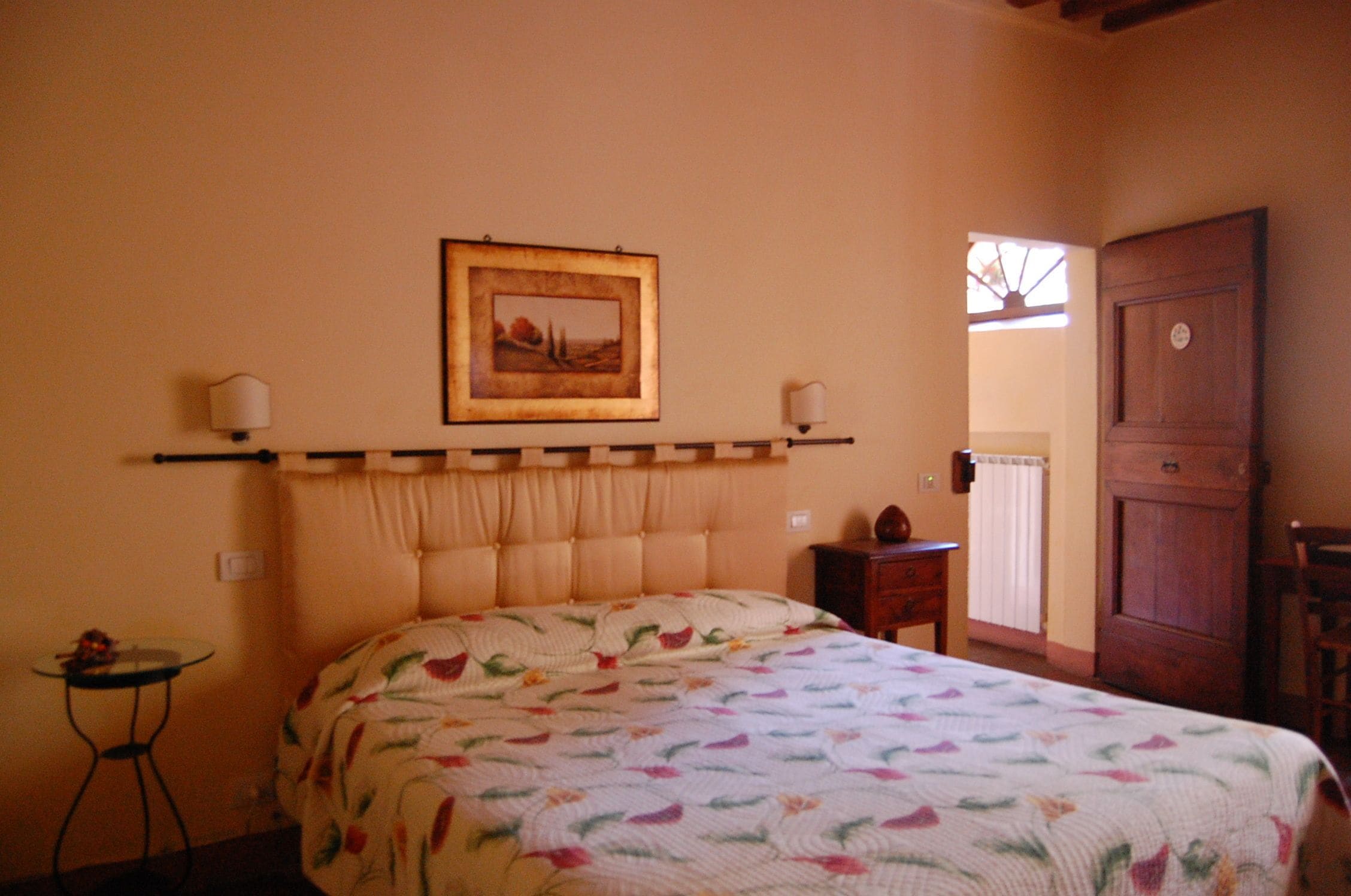 Een slaapkamer met een groot bed, een ingelijst kunstwerk aan de muur, een klein tafeltje en een houten kast.