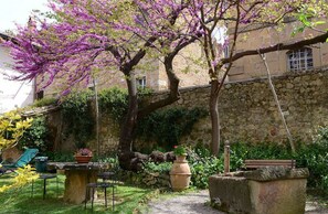 A stone wall, a bench, and a table with chairs in a garden. - Il Giardino Segreto (Pienza)