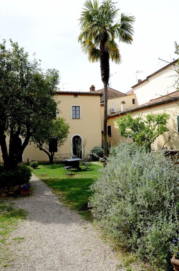 A courtyard with a palm tree, a gravel path, and a building with a door and windows. - Il Giardino Segreto (Pienza)
