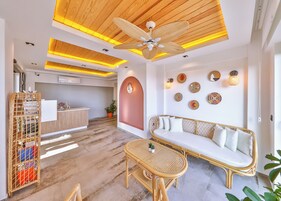 Un área de recepción con un mostrador de madera, un sofá de mimbre, una mesa de mimbre y un ventilador de techo.