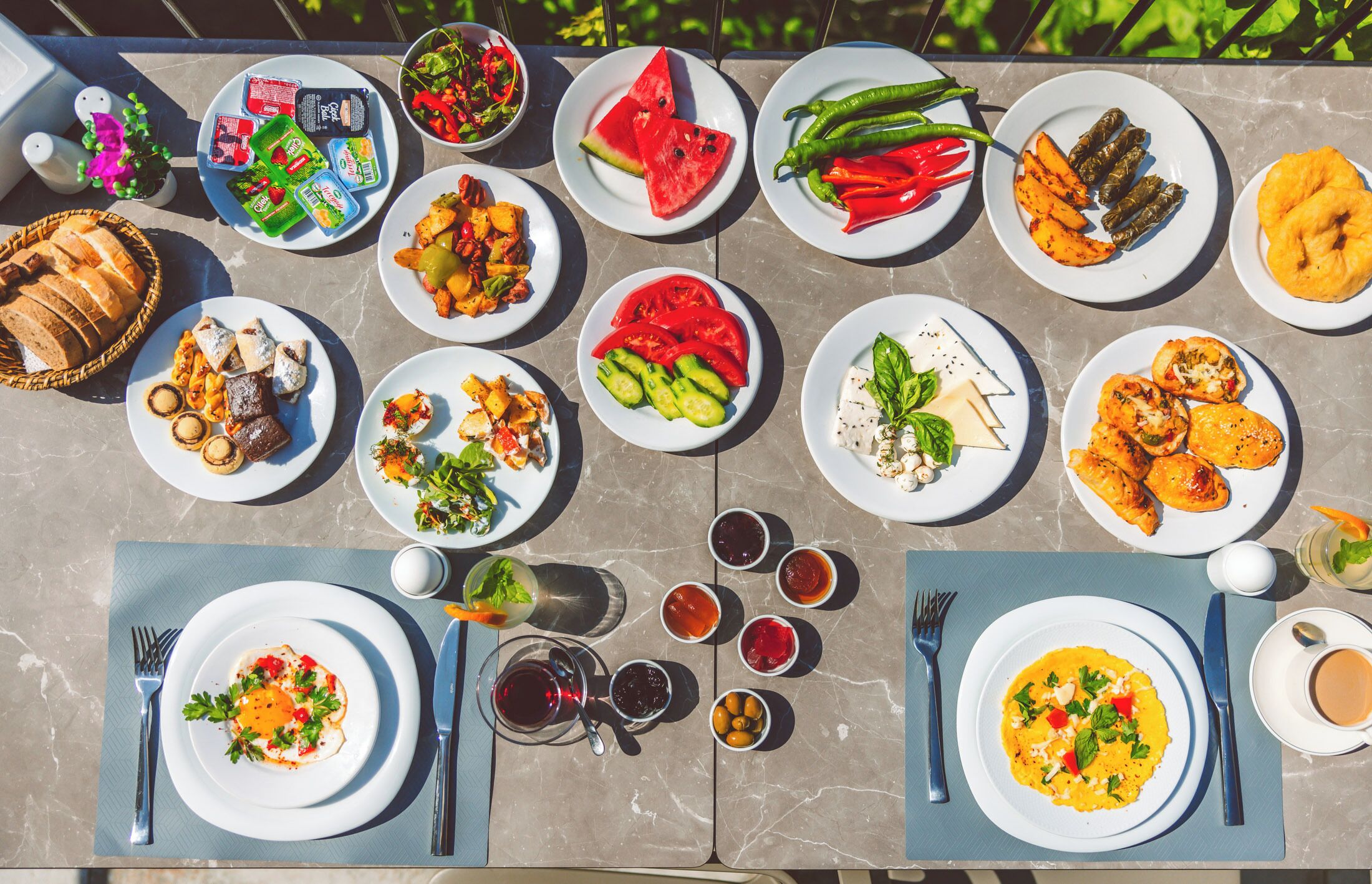 A table set with various dishes, including salads, meats, and desserts, arranged on a marble table outdoors.