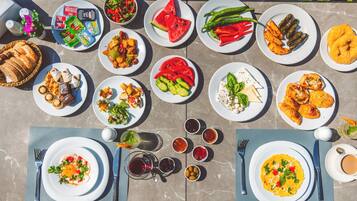 A table set with various dishes, including salads, meats, and desserts, arranged on a marble table outdoors.
