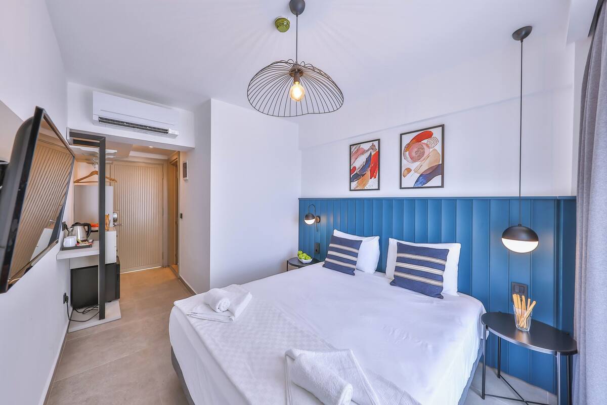 A modern hotel room with a large bed, a desk with a chair, a flat-screen TV, and a ceiling fan.