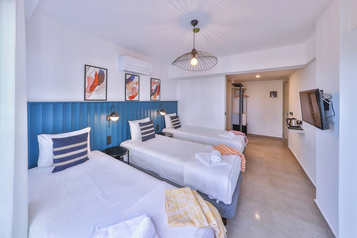 A hotel room with three beds, a TV, and a kitchenette.