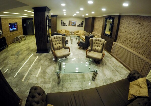 A lobby with a glass-top coffee table surrounded by armchairs, a sofa, and a TV screen displaying a news channel. - Keles Hotel (Rize)