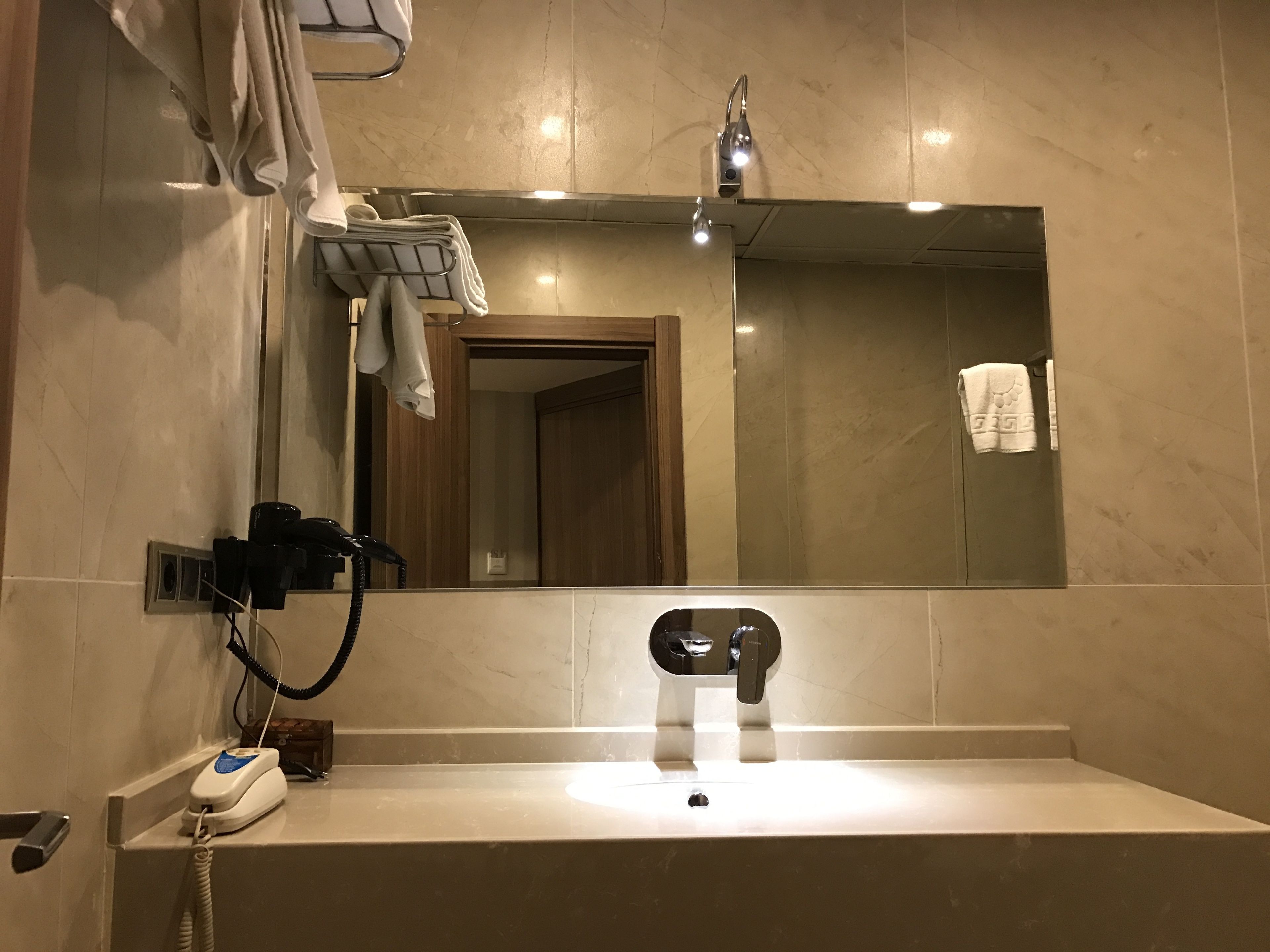 A bathroom with a large mirror, a sink, a hairdryer, and a towel rack.