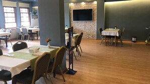 A spacious dining area with multiple tables and chairs, a stone accent wall, and a flat-screen TV mounted above the seating area. - Keles Hotel (Rize)