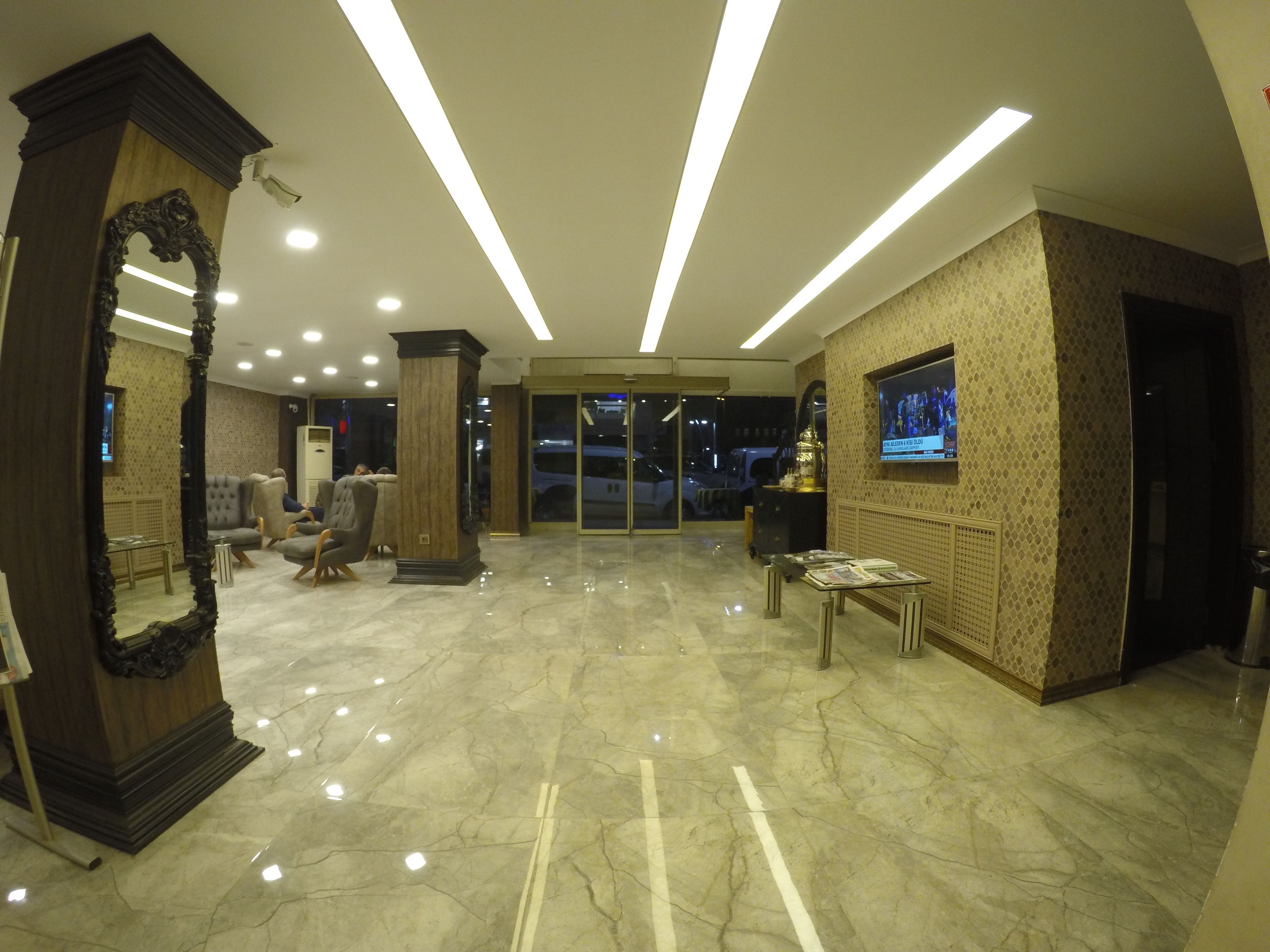 A hotel lobby with a marble floor, a large mirror, seating area, and a television screen.