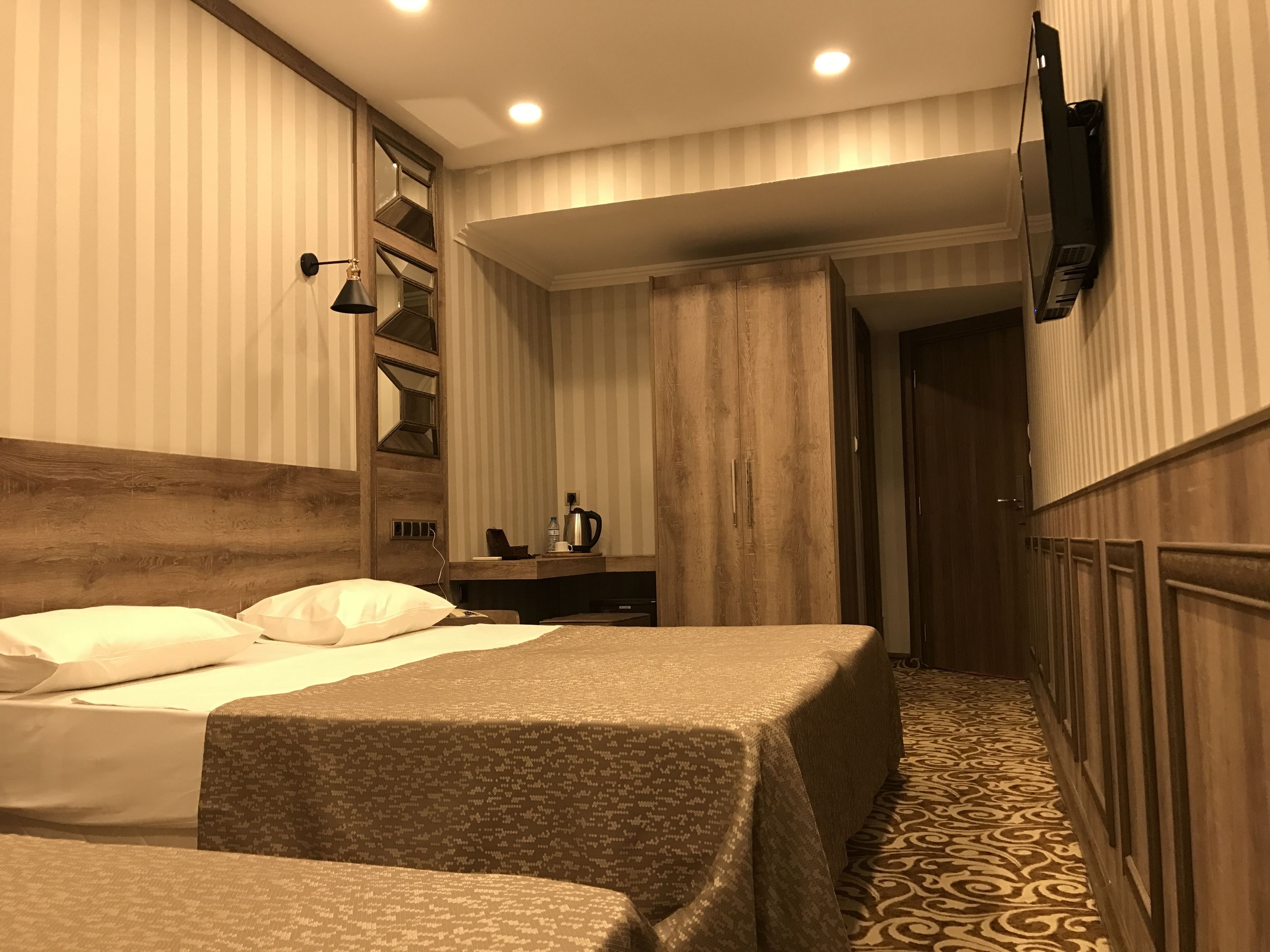 A hotel room with two beds, a desk, a TV, and a patterned carpet.