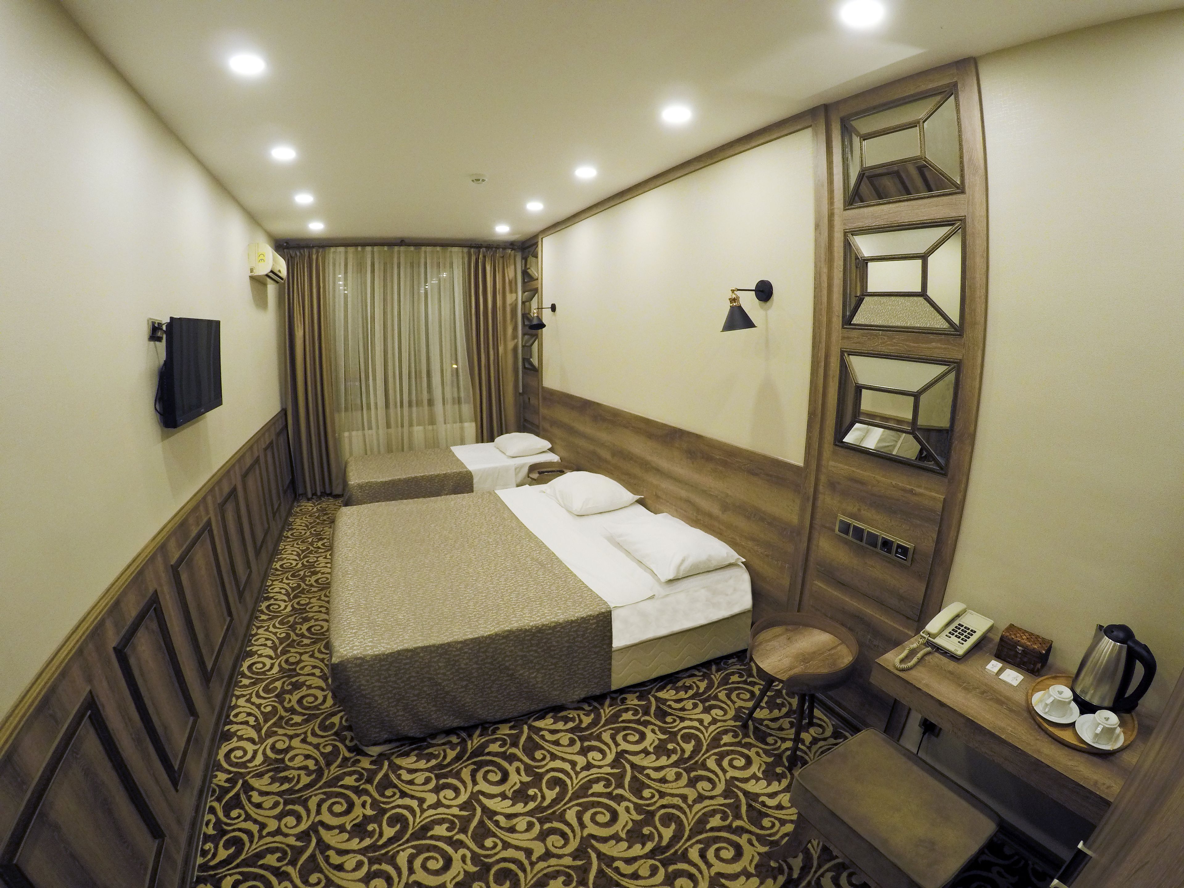 A hotel room with two beds, a desk with a telephone and a coffee maker, a mirror, and a patterned carpet.