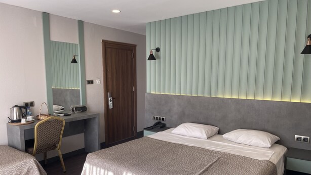 A hotel room with a bed, a desk, a chair, a wardrobe, and a mirror. - Keles Hotel (Rize)