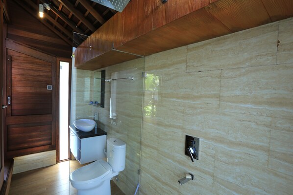 A modern bathroom with a wooden door, a white sink, and a glass shower enclosure.