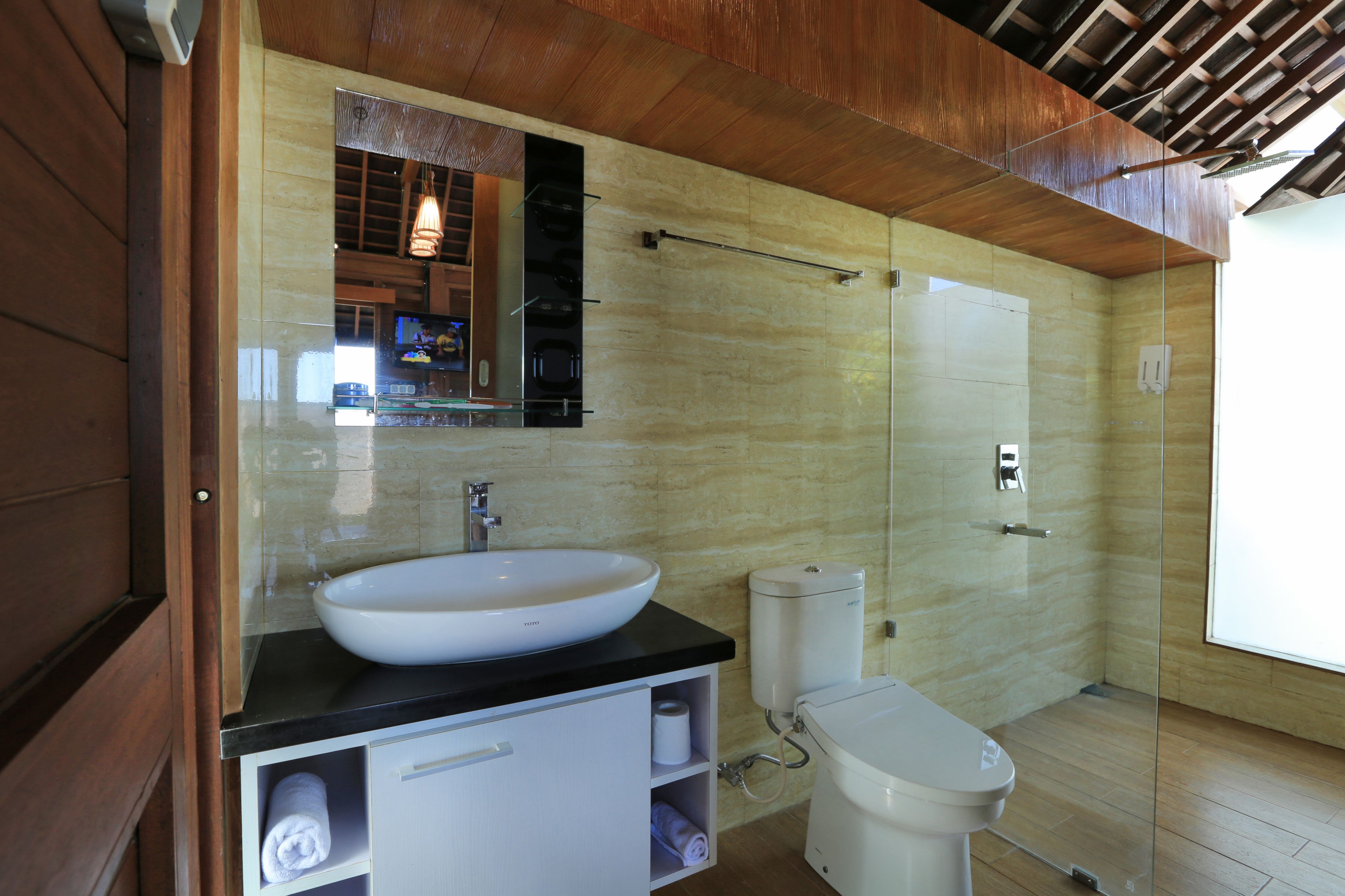 A modern bathroom with a large white sink, a toilet, and a glass-enclosed shower.
