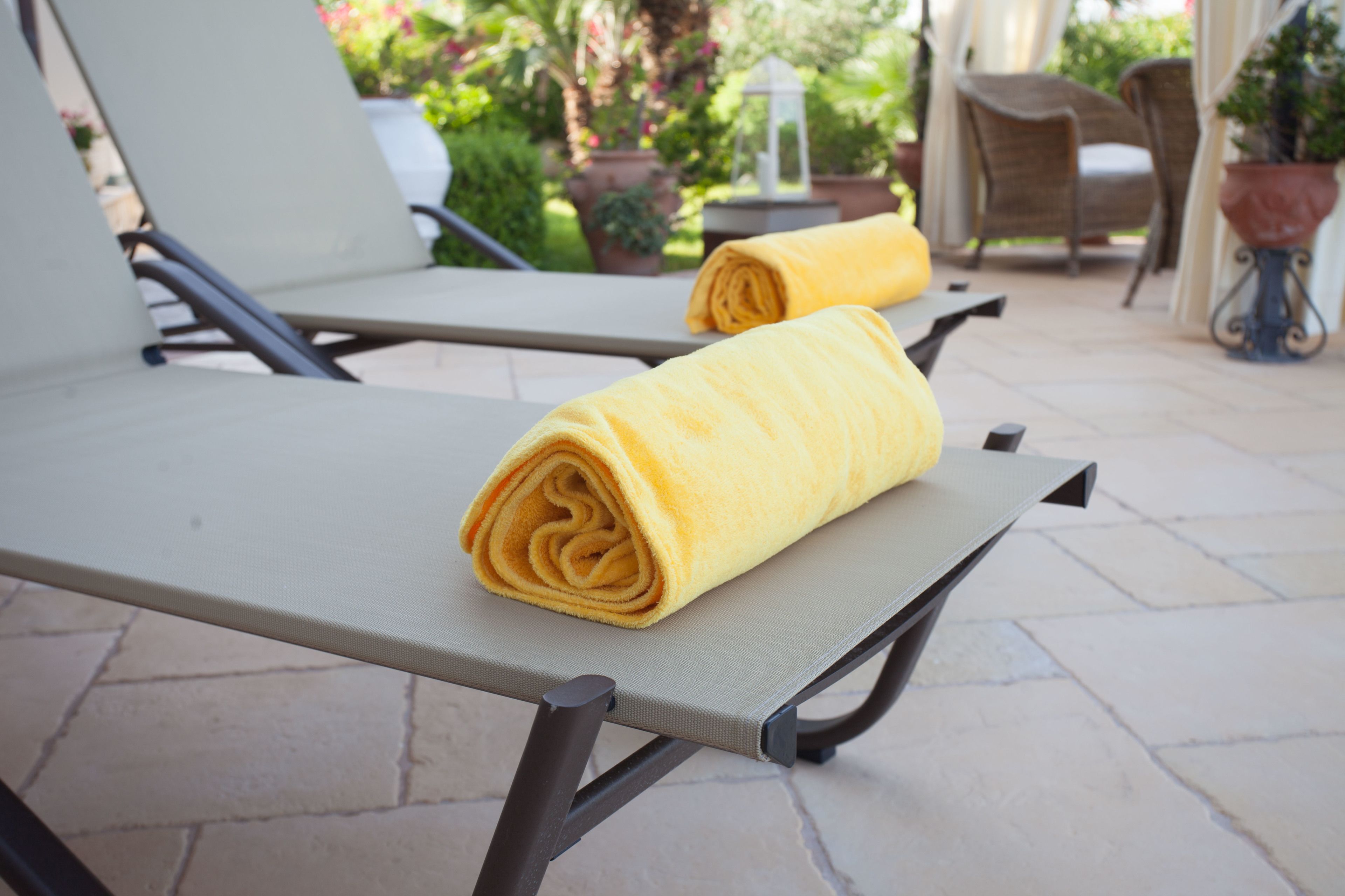 Two lounge chairs with yellow towels, a stone patio, and outdoor furniture.
