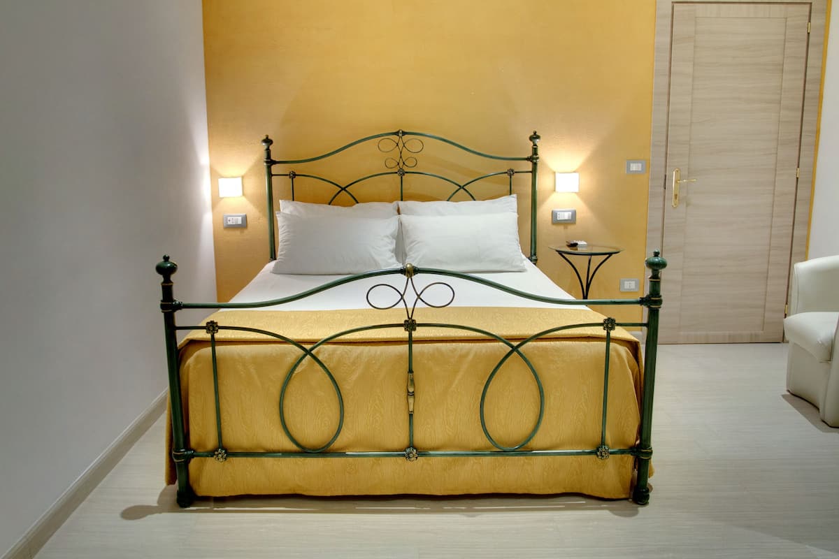 A bed with a metal frame and a yellow bedspread in a room with yellow walls and a wooden door.