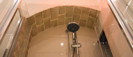 A shower area with a stone-tiled wall and a chrome showerhead.