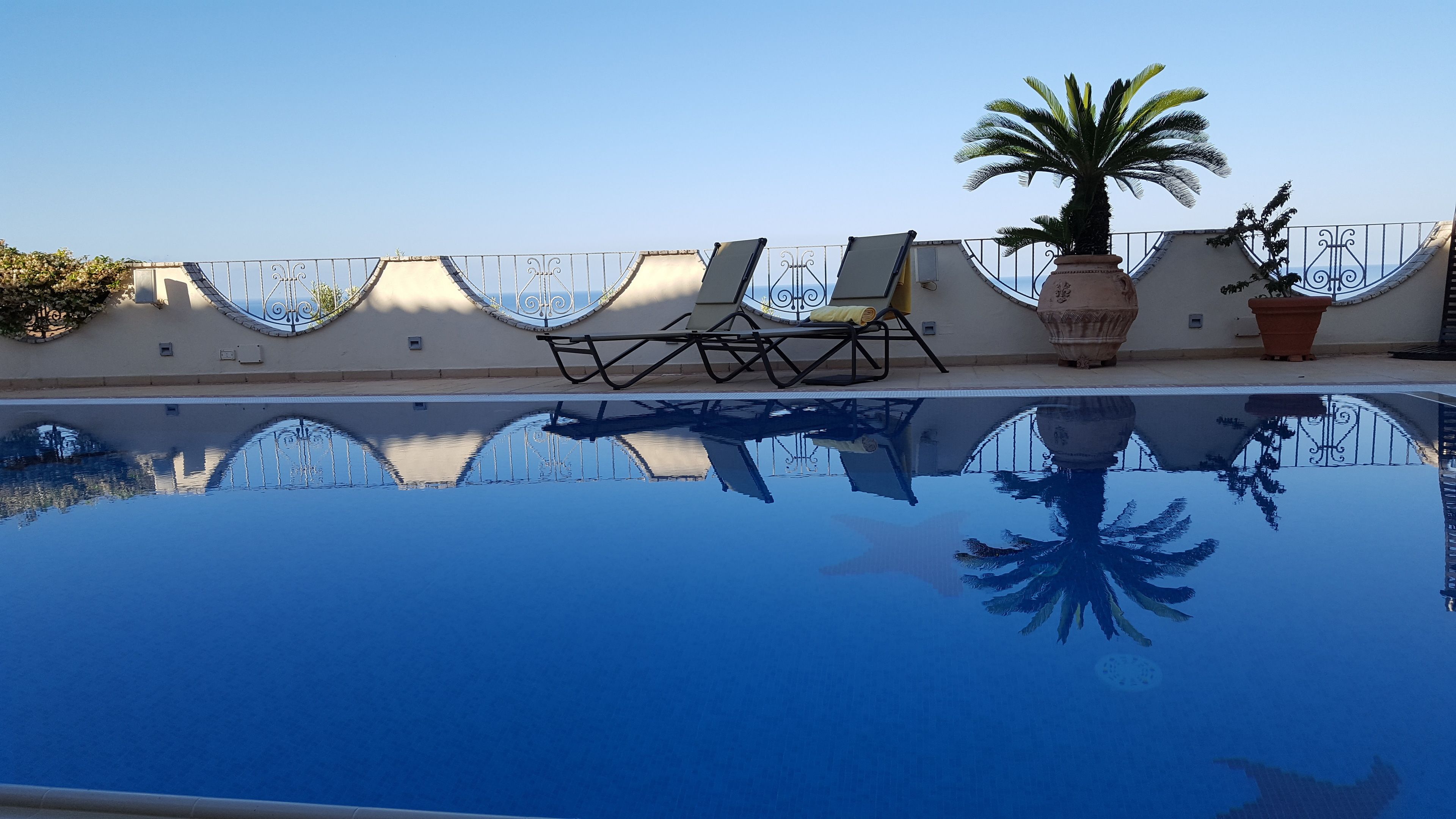 Una piscina azul cristalina con sillas de descanso y plantas en macetas.