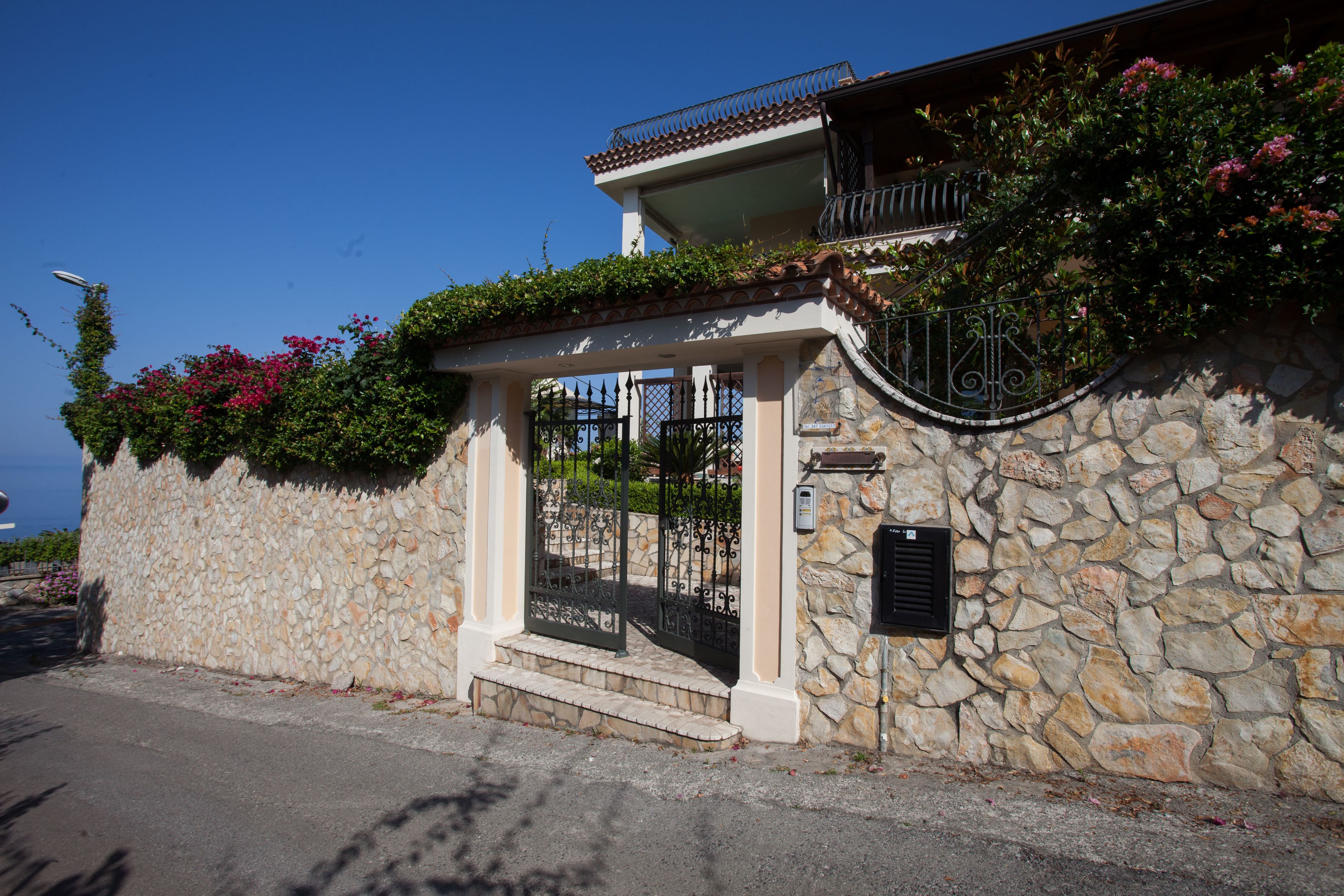 A stone-walled building with a gated entrance, a balcony, and a stone staircase leading to the entrance.