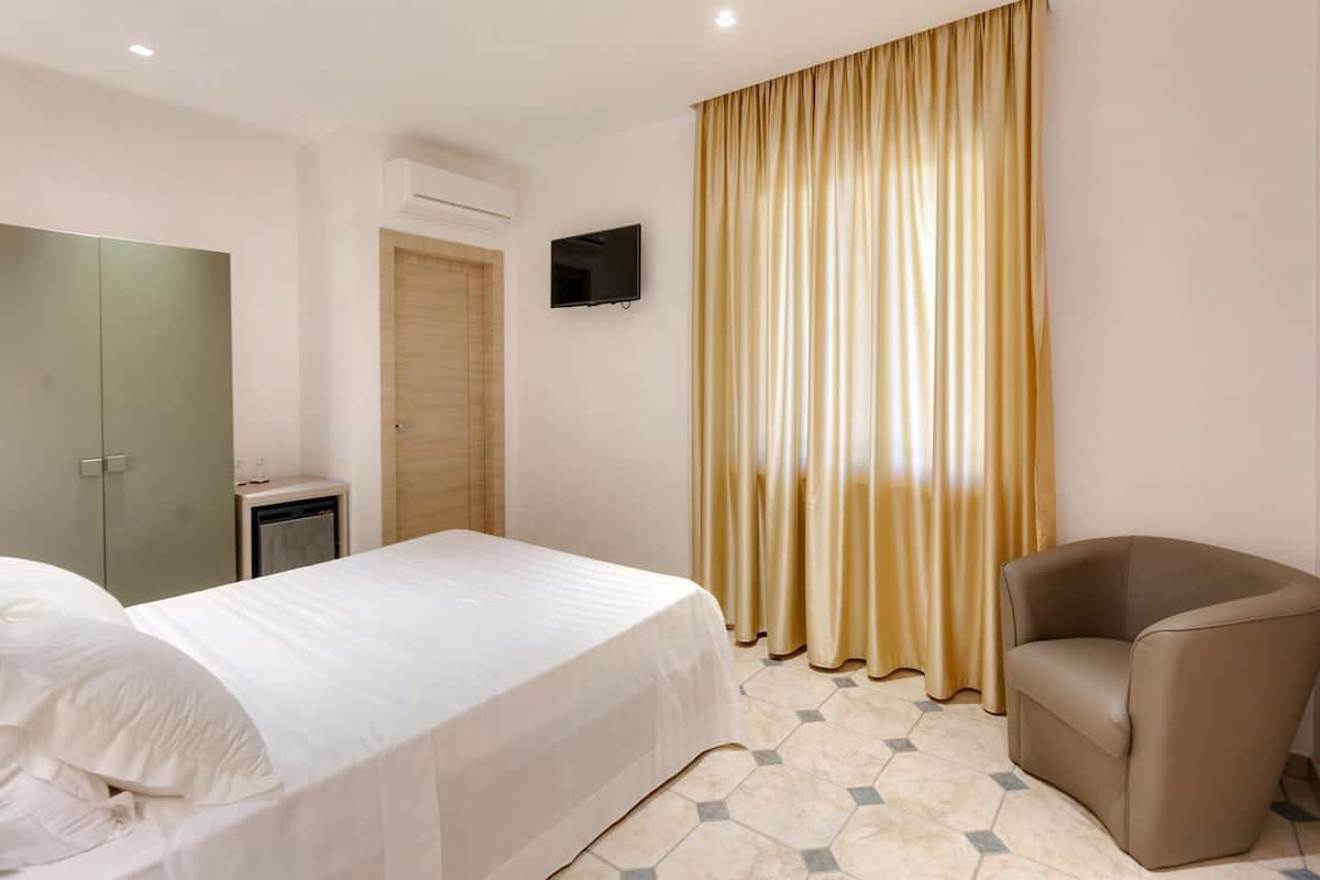 A hotel room with a bed, a chair, a television on the wall, and a window with curtains.