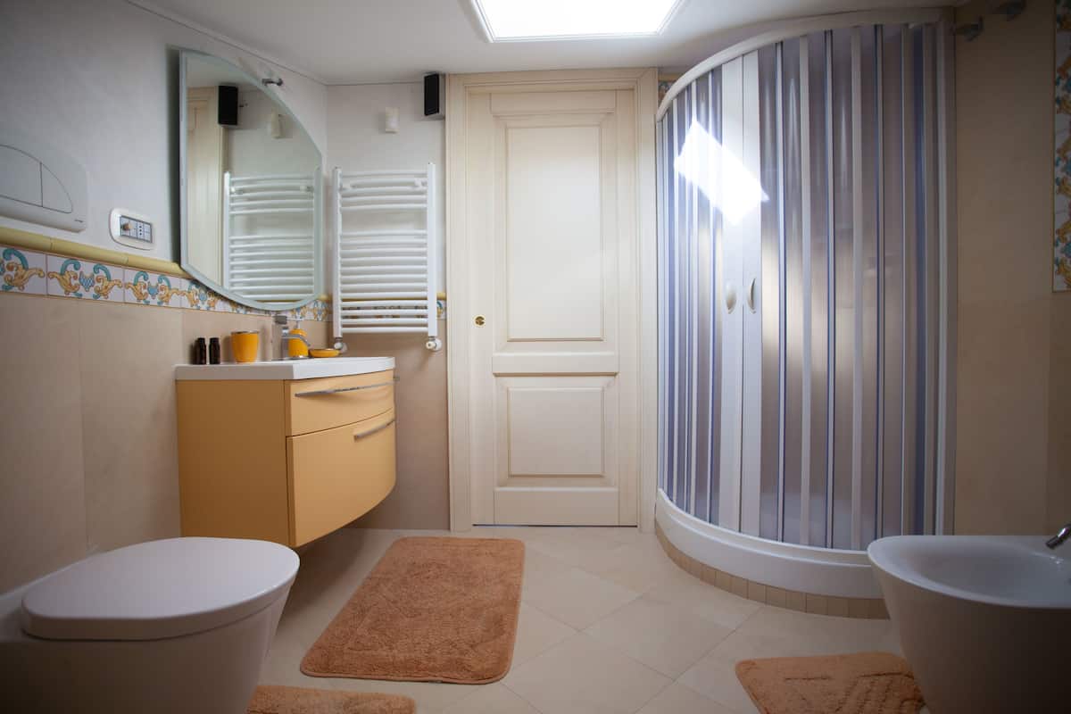 A bathroom with a toilet, sink, mirror, shower, and a door.