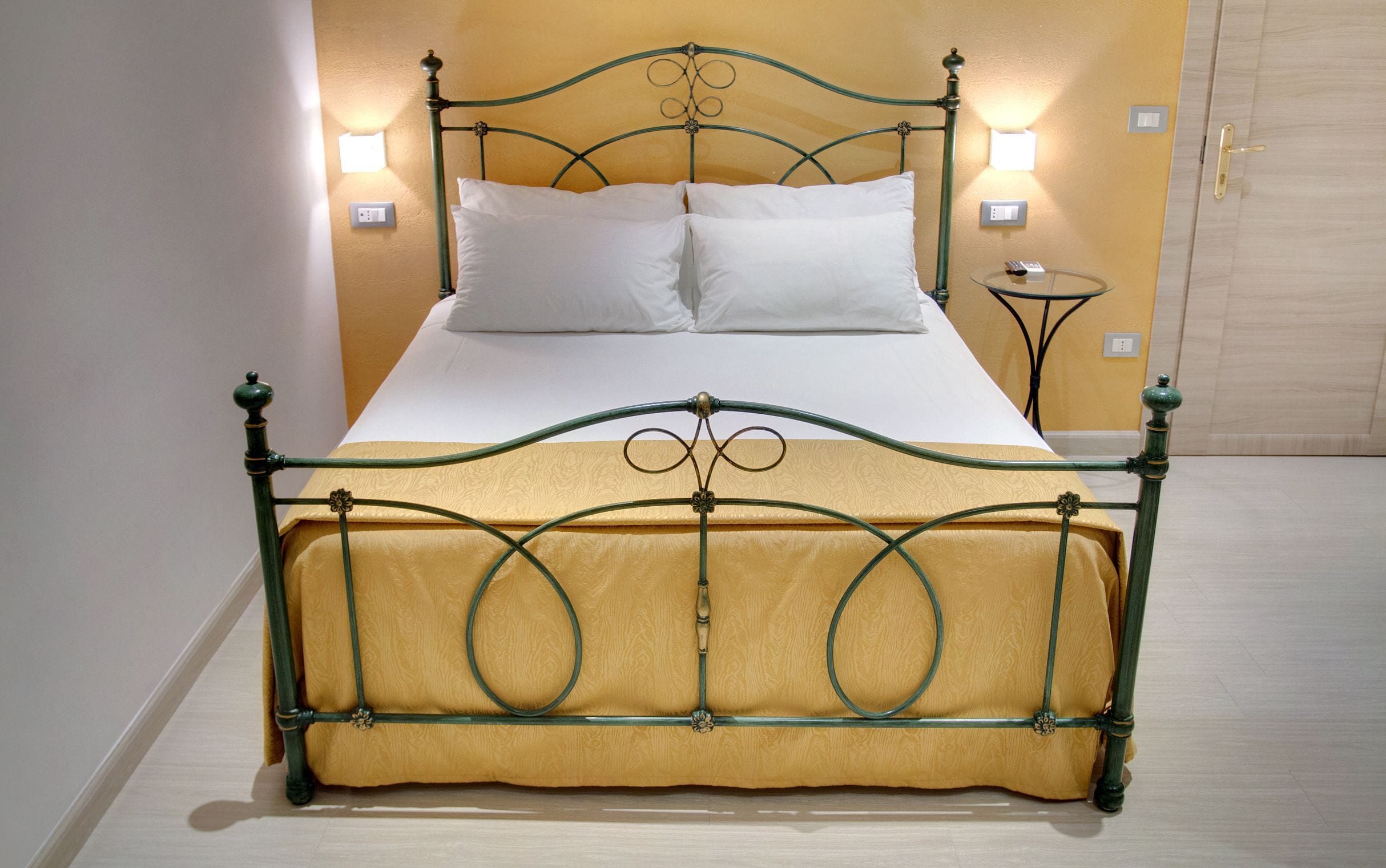 A bed with a green metal frame and a yellow upholstered headboard. There are two bedside tables with lamps on either side of the bed.