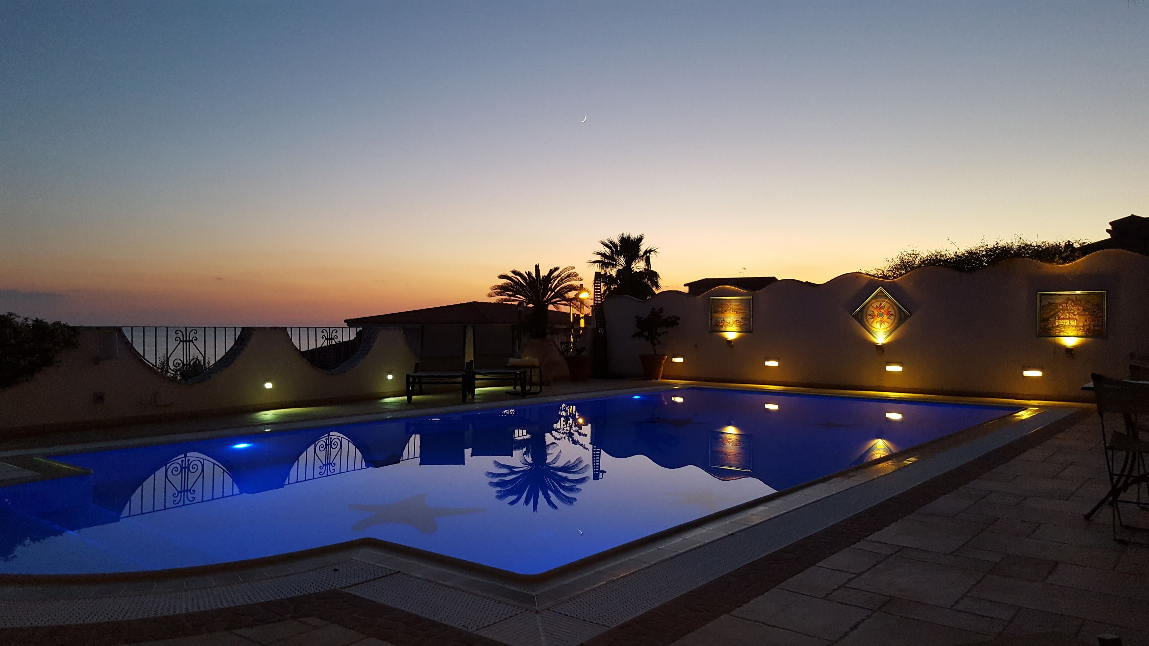 Una piscina con vista al atardecer, rodeada de un patio con sillas y un banco.