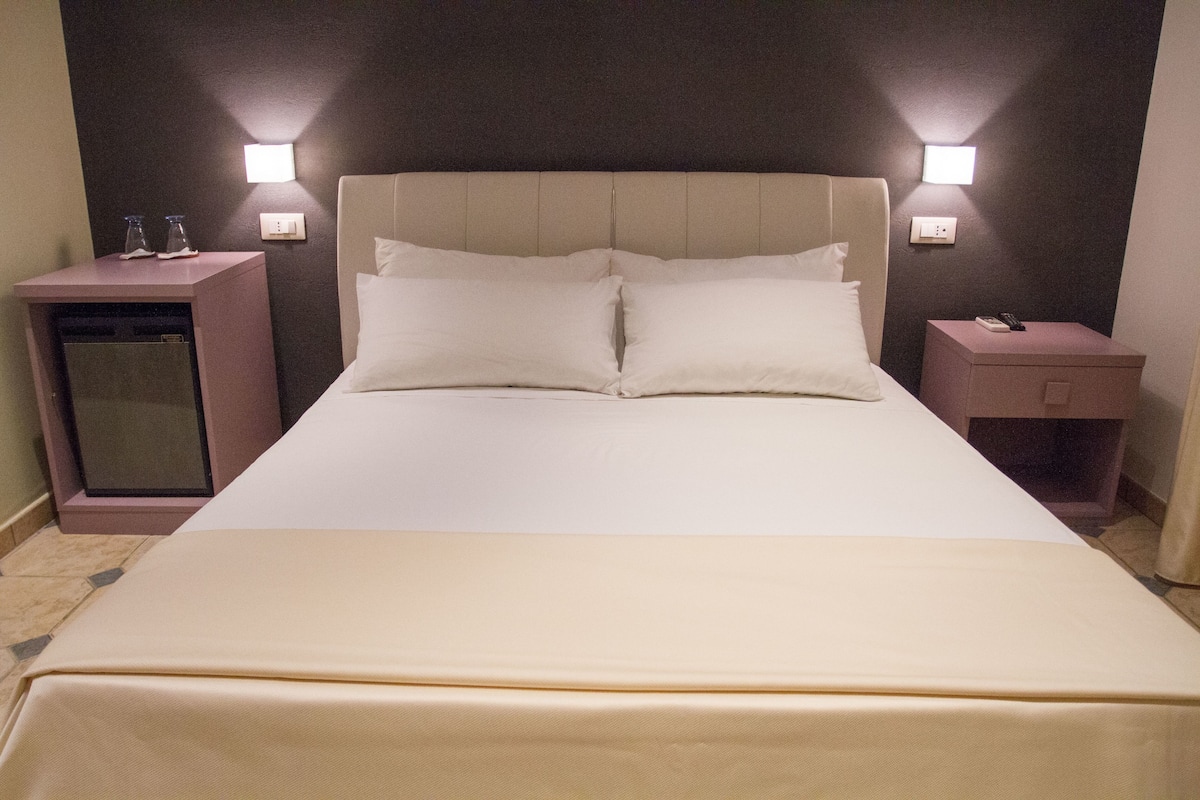 A hotel room with a large bed, two bedside tables, and wall-mounted lights.