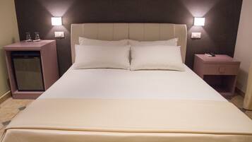 Una habitación de hotel con una cama grande, dos mesitas de noche y luces fijadas a la pared.