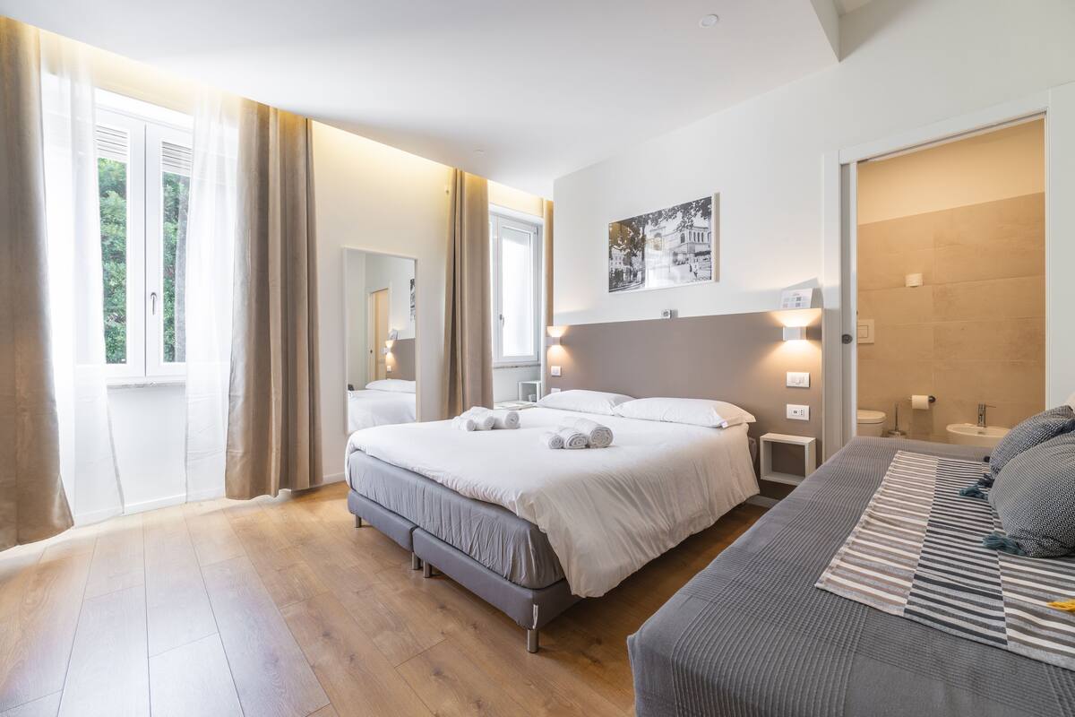 A modern bedroom with a large bed, bedside tables, a bedside lamp, and a window with curtains.