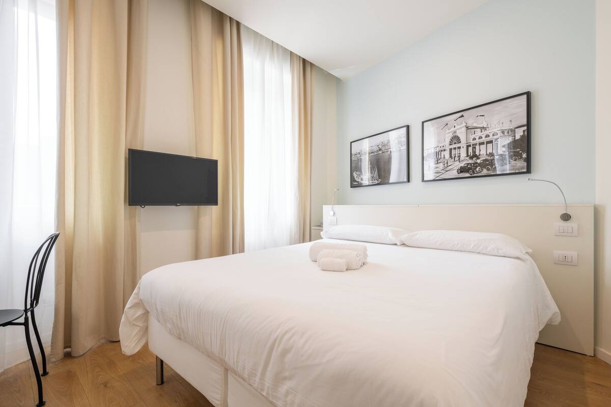A hotel room with a bed, a TV mounted on the wall, and two framed pictures above the bed.