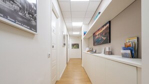 A hallway with a wooden floor, white walls, and a reception desk with magazines and a painting. - Dome (Cagliari)