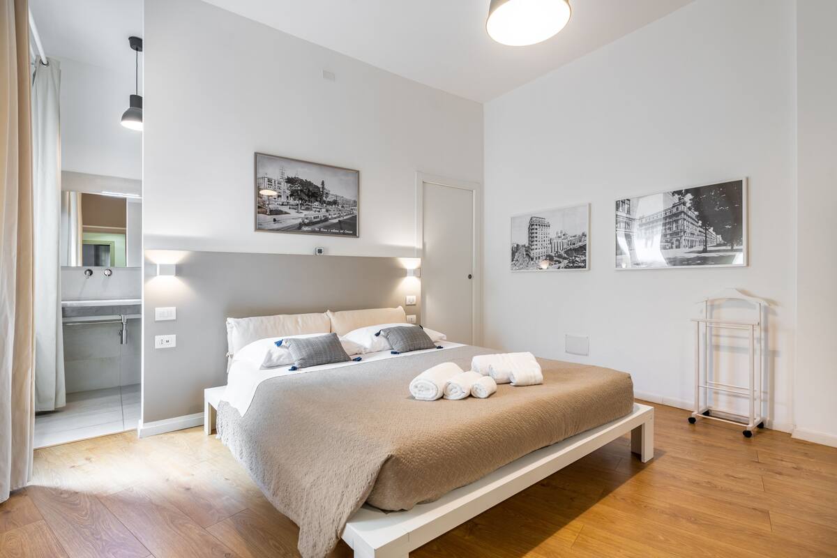 A modern bedroom with a large bed, a bedside table, a mirror, and artwork on the walls.