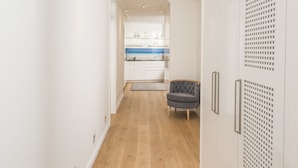 Un pasillo moderno con suelo de madera, paredes blancas y un sillón gris.