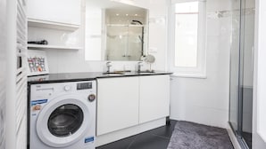 Un baño moderno con lavadora, cabina de ducha de vidrio y un espejo grande.