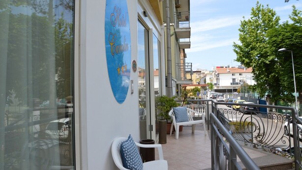 Un hotel con un letrero azul, zona de estar al aire libre con sillas y una mesa, y vistas a la calle y edificios al fondo.