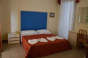 A hotel room with a single bed, a nightstand, a desk, and a chair. - Hotel Carolin (Rimini)