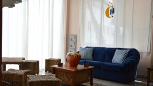 Una sala de estar con un sofá azul, muebles de mimbre, una mesa de centro de madera con un jarrón de flores y una alfombra estampada.