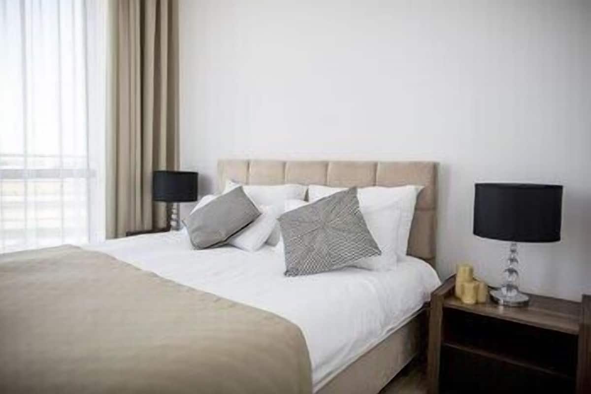 Ein Hotelzimmer mit einem Bett, zwei Nachttischen, einer Lampe und einem Fenster mit Vorhängen.