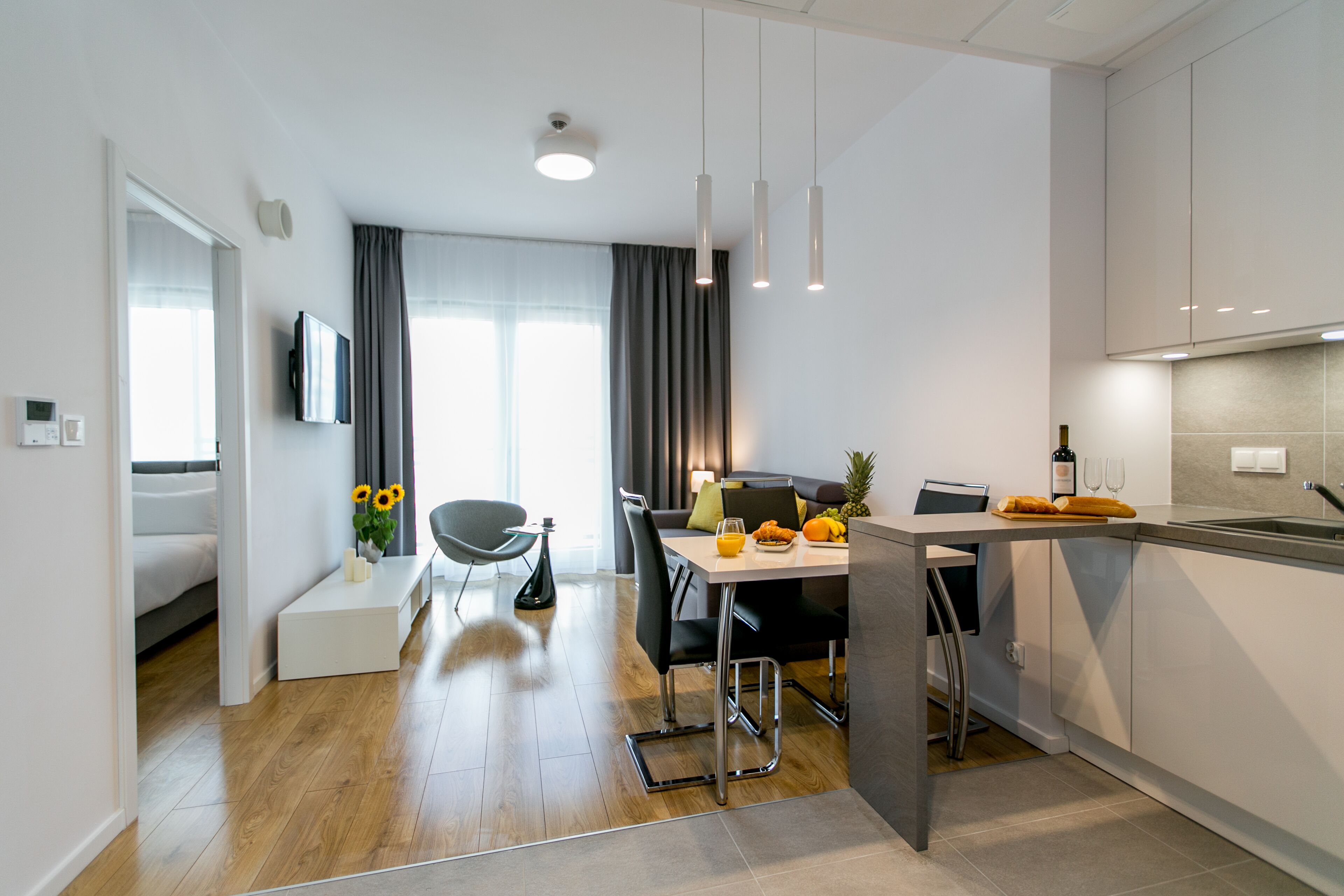 A modern kitchen with a dining area, wooden flooring, and a view of the living room.