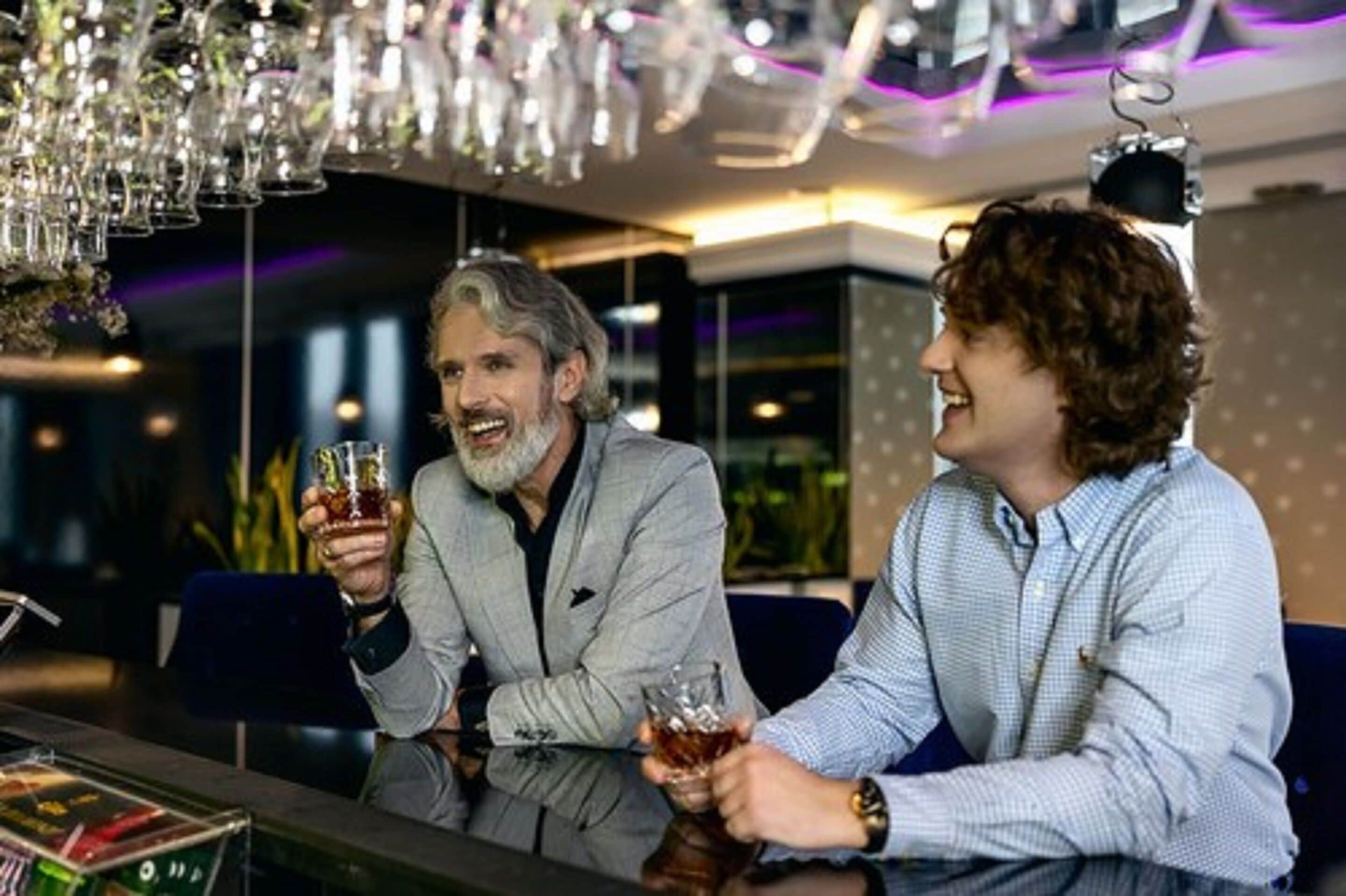 Zwei Personen sitzen an einer Bar mit modernem Ambiente, darunter hängendes Glasgeschirr und eine gute Beleuchtung.