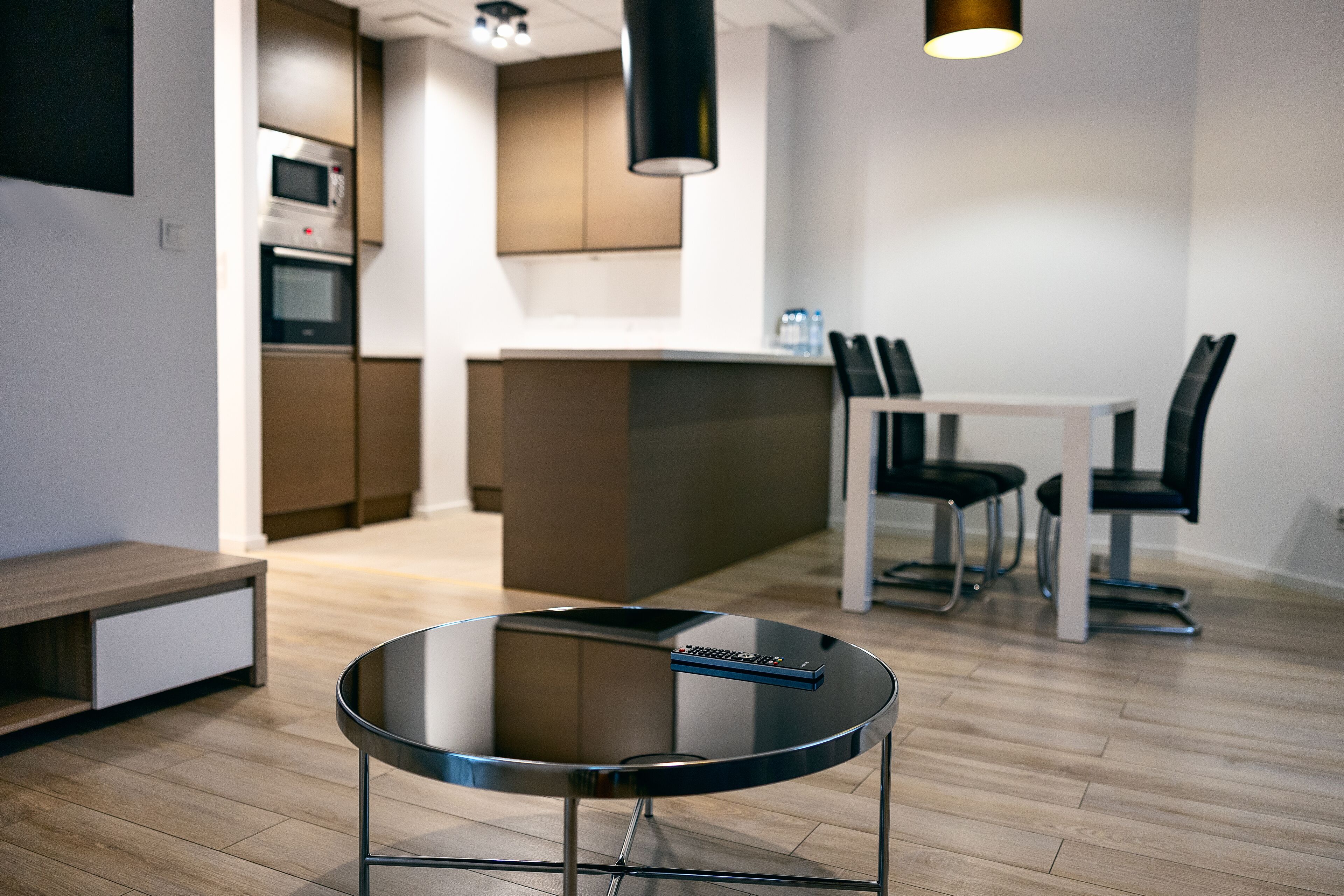 Une cuisine moderne dotée d’appareils électroménagers intégrés, un coin repas avec une table et des chaises, et une table ronde en verre aux pieds métalliques, placée au premier plan.
