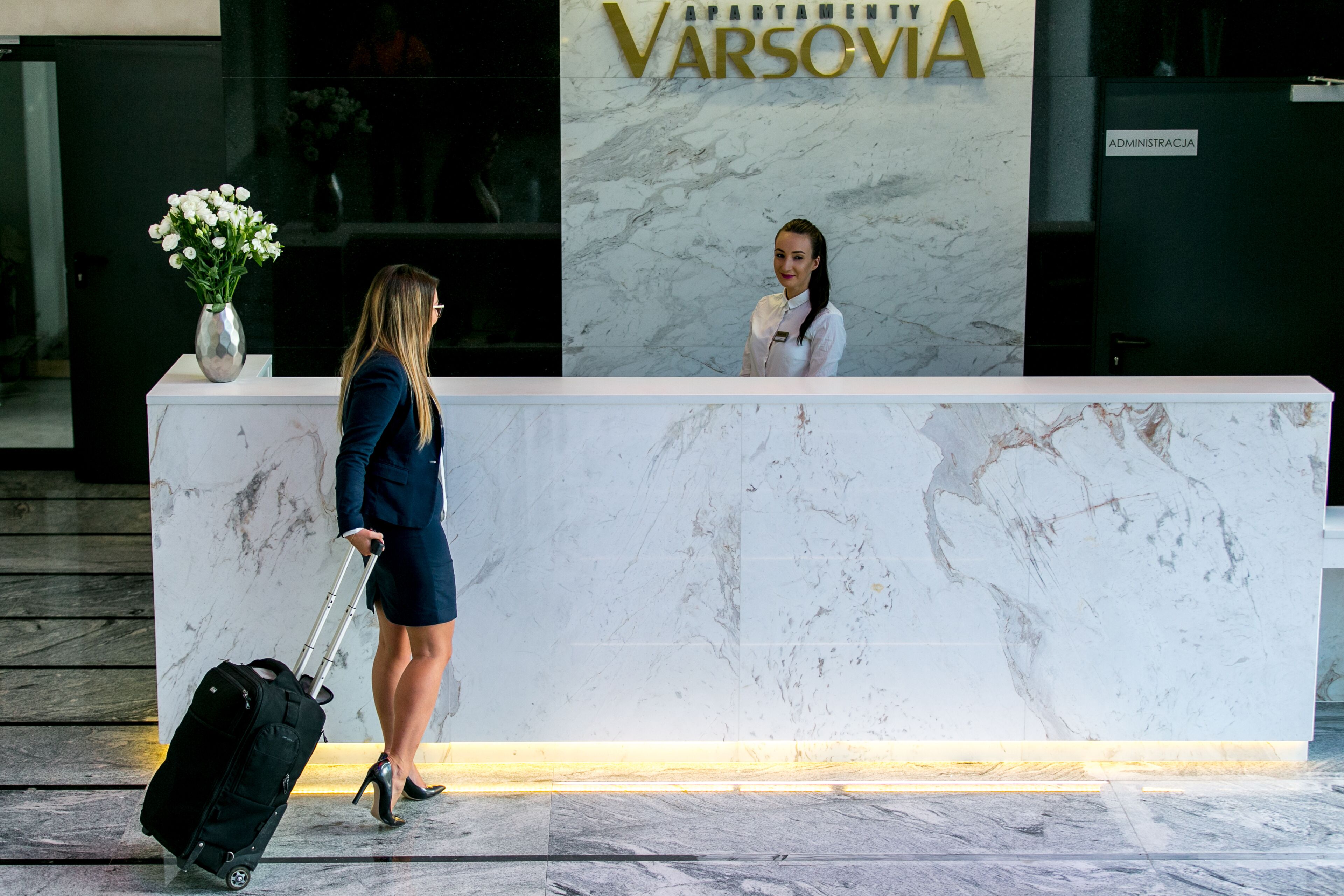 Ein Empfangsbereich mit Marmorverkleidung, einer Vase mit weißen Blumen und einem Schild mit der Aufschrift 'VARSOVIA'.