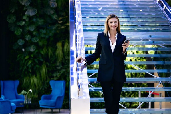 A person in business attire standing next to a modern, glass staircase with a metal railing. - Varsovia Apartamenty Kasprzaka (Warsaw)