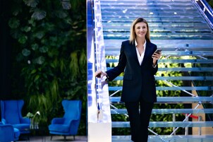 Una persona vestida con traje de negocios parada junto a una moderna escalera de cristal con barandilla metálica.