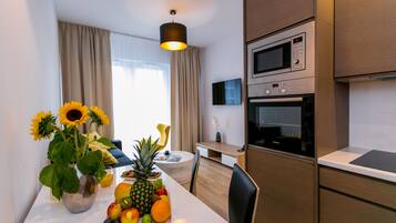 A modern kitchen with a microwave, oven, and a dining area with a fruit bowl and a vase of sunflowers.
