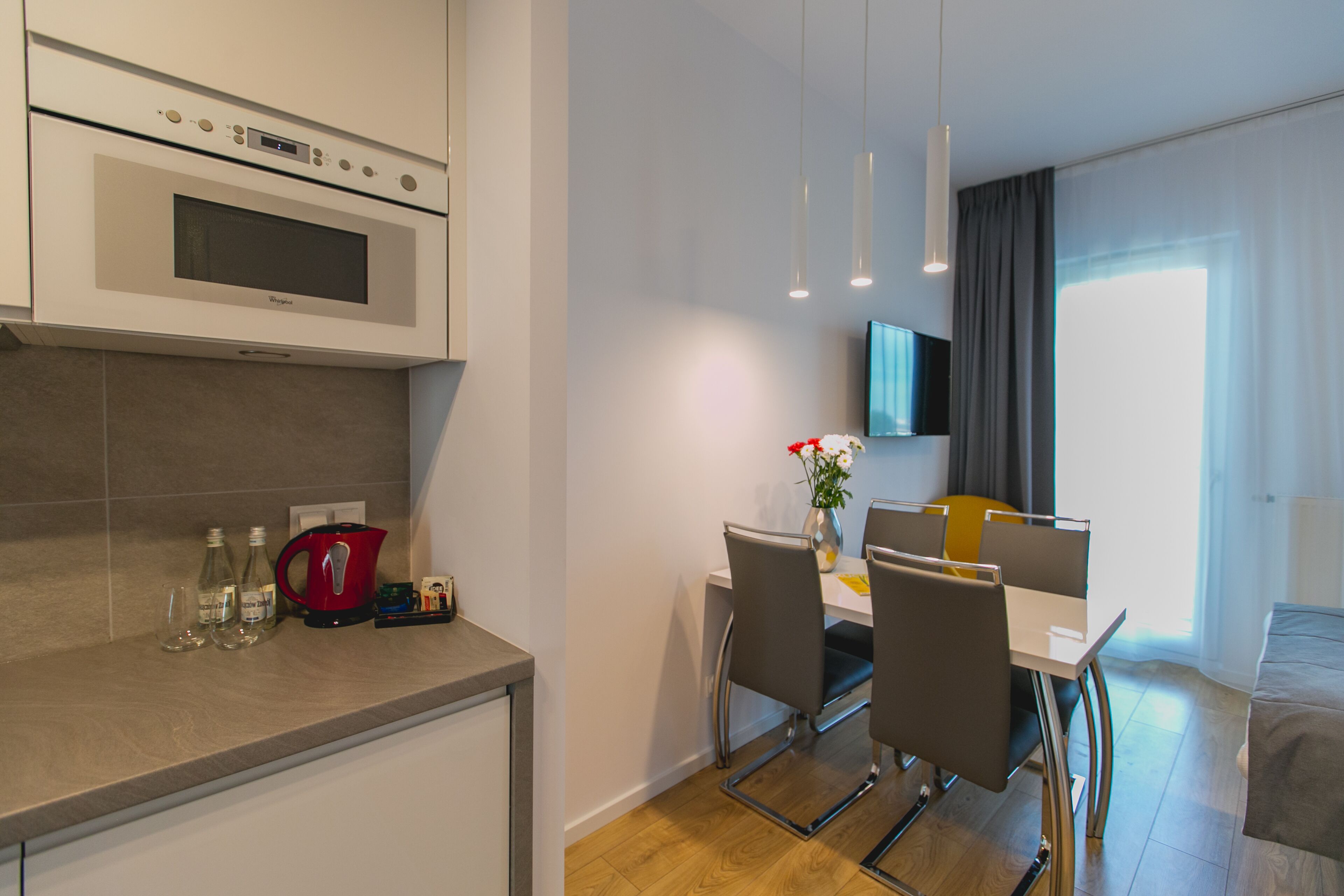 Una cocina moderna con horno integrado, un comedor con mesa y sillas, y un televisor de pantalla plana montado en la pared.