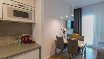 Una cocina moderna con horno integrado, un comedor con mesa y sillas, y un televisor de pantalla plana montado en la pared.